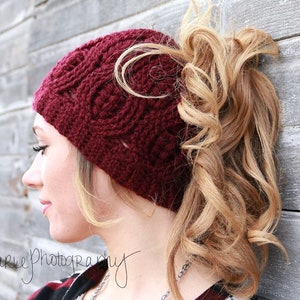 May include: A burgundy crocheted hat with a ponytail hole. The hat has a delicate, lacy design.