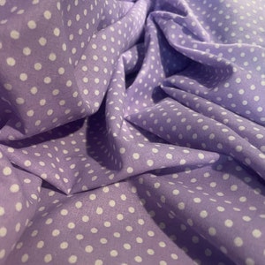May include: Purple fabric with white polka dots. The fabric is folded and draped.