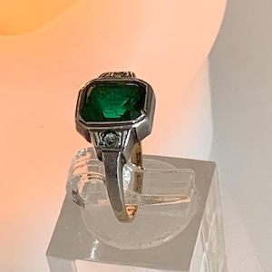 Op de afbeelding: Een zilveren ring met een groene smaragd edelsteen en kleine diamant accenten.