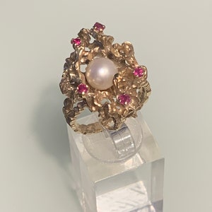 May include: A gold ring with a pearl and red gemstones set in a textured, organic design.