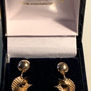 May include: A pair of gold earrings with a twisted design. The earrings are in a black box with the text "SIMON MILNE RYE www.simonmilne.co.uk".