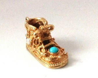 Op de afbeelding: Een gouden bedel in de vorm van een babyschoen met een turquoise steen en parel accenten.