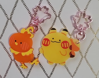May include: Two cartoon character keychains. One is orange and yellow, resembling a chick. The other is yellow with red accents, resembling a mouse. Both have pink flower-shaped clasps.