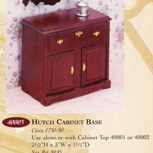 May include: A miniature mahogany hutch cabinet base with a drawer and two doors, adorned with gold-colored hardware. A small silver container sits atop the cabinet. The cabinet measures 2.5"H x 3"W x 1.5"D. The text on the image reads "Hutch Cabinet Base".