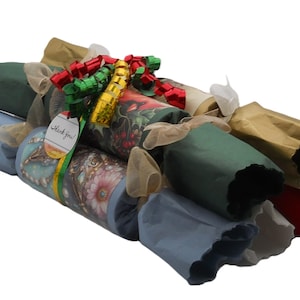 Peut inclure: Un ensemble de papillotes cylindriques emballées dans des papiers de différentes couleurs, notamment bleu clair, vert foncé, doré et rouge. Elles sont nouées avec des rubans transparents et un nœud décoratif, avec une étiquette Thank You.