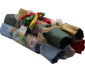 May include: A collection of cylindrical paper crackers in various colors including green, blue, gold, and red, tied together with sheer ribbons and a shiny red, green, and gold bow. A small white tag attached to the ribbons features the text Thank You.