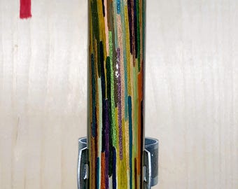 May include: A close-up of a wooden dowel with a pointed tip, painted with colorful stripes in shades of green, yellow, orange, red, blue, and purple. The dowel is secured with a metal ring.