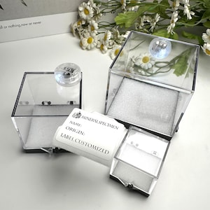 May include: Clear acrylic display boxes with hinged lids. Each box contains white foam padding. A label reads "MINERAL SPECIMEN" with space for name, origin, and customized label information. The boxes are designed to showcase small items.