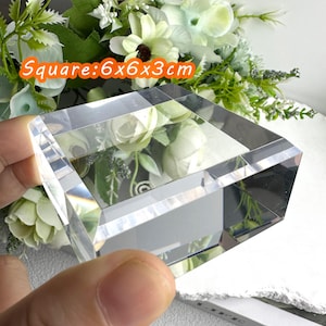 Puede incluir: Un bloque de cristal transparente y cuadrado, de 6 x 6 x 3 cm, con un dise&ntilde;o facetado. El texto "Square: 6x6x3cm" es visible. El fondo presenta flores blancas y verdes.