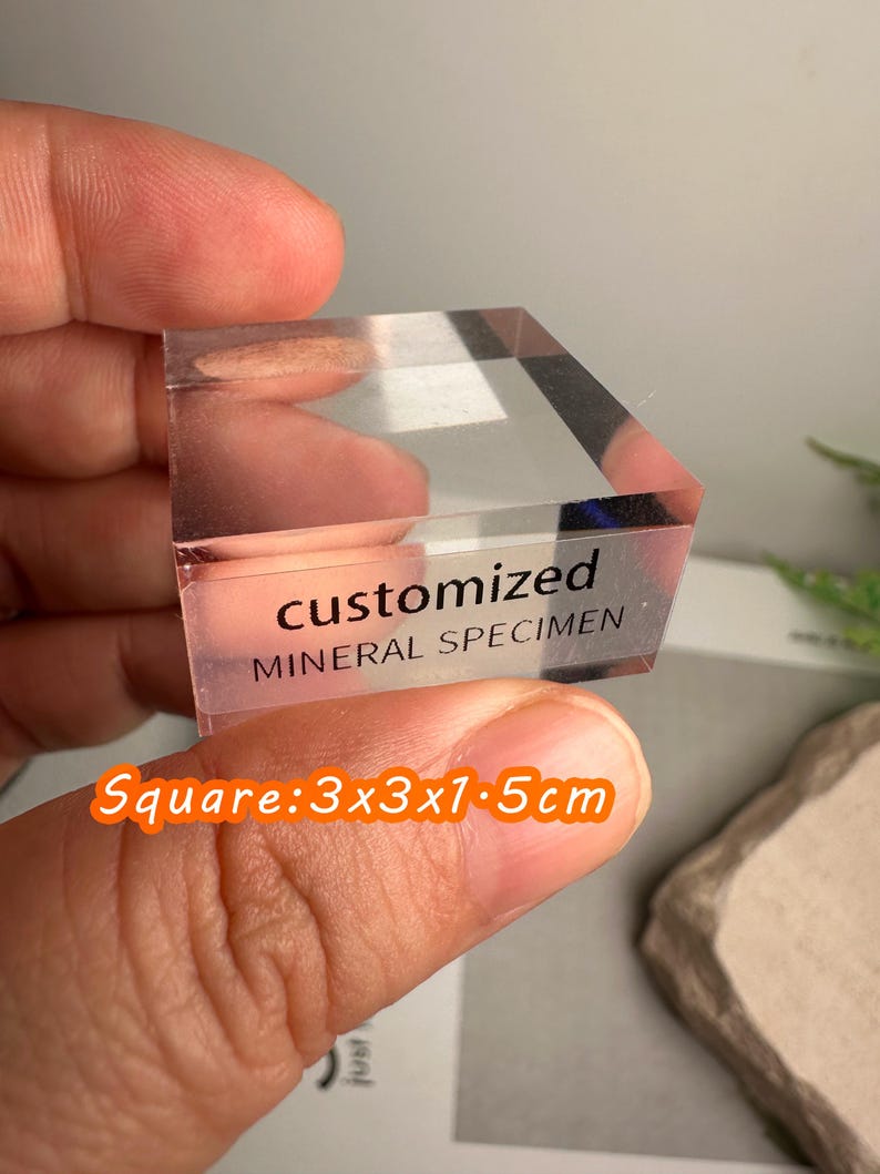 Puede incluir: Un esp&eacute;cimen mineral transparente y cuadrado con el texto "customized MINERAL SPECIMEN". Mide 3x3x1,5 cm. El esp&eacute;cimen se sostiene entre los dedos. Tambi&eacute;n se ve el texto "Square: 3x3x1.5cm".