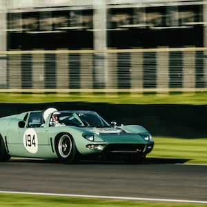May include: A green vintage race car with the number 194 on the side, driving on a race track.