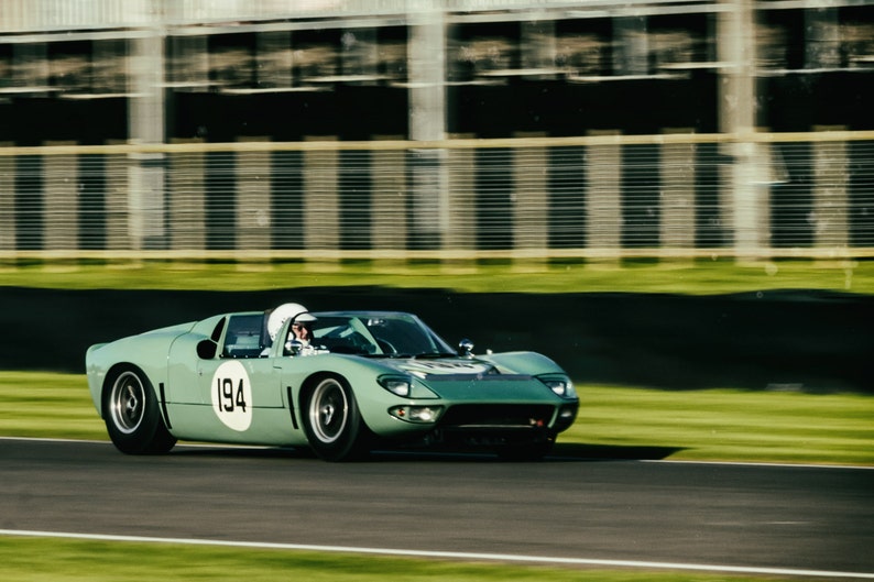 May include: A green vintage race car with the number 194 on the side, driving on a race track.