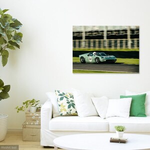 May include: A vintage green race car with the number 54 on the side, driving on a race track. The car is in motion, and the background is blurred.