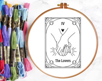 Puede incluir: Un aro de bordado en blanco y negro con un diseño de la carta del tarot de Los Enamorados. La carta presenta dos manos que se sostienen, con un corazón encima. El número de la carta, IV, y las palabras "Los Enamorados" también están incluidas en el diseño.