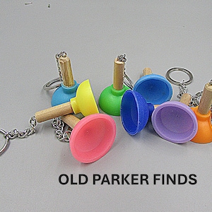 May include: A set of six colorful miniature plunger keychain charms. The plungers are made of rubber and have wooden handles. The keychains are attached to silver metal rings.