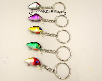 May include: Five colorful fishing lure keychains with silver key rings. The lures are silver, purple, yellow, green, and red.