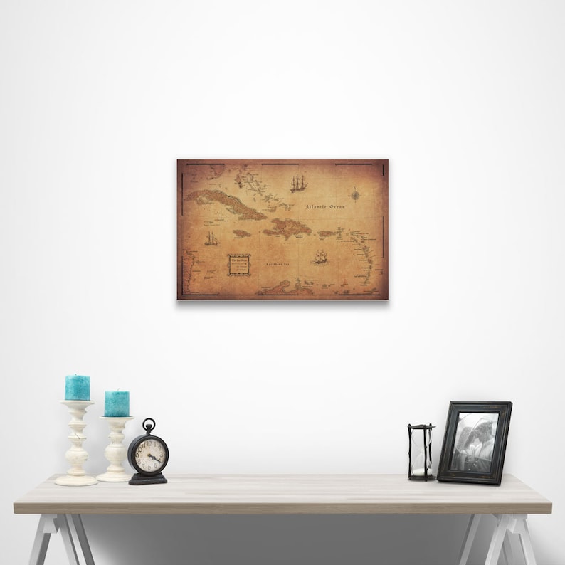 May include: A vintage-style map of the Caribbean islands with the text "Atlantic Ocean" printed on the map. The map is printed on a brown background with a distressed look. The map is framed and hanging on a white wall.
