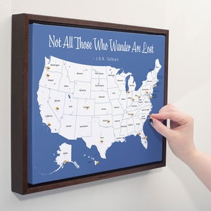 May include: A blue canvas map of the United States with gold push pins marking locations. The map is framed in a dark wood frame. The text "Not All Those Who Wander Are Lost - J.R.R. Tolkien" is printed at the top of the map.