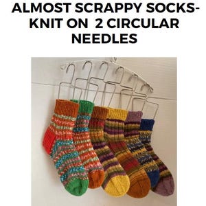 May include: Five pairs of colourful striped socks knitted on two circular needles. The socks are hanging on a metal rack. The socks are made with a variety of colours, including orange, yellow, green, blue, and purple.
