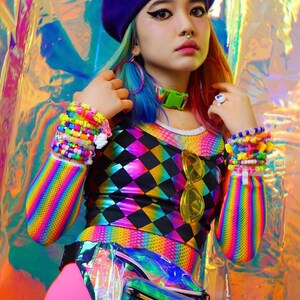 May include: A woman wearing a rainbow striped long-sleeved shirt with a black and rainbow diamond pattern top. She is wearing a purple beret with a green alien graphic, a rainbow beaded bracelet, and a clear iridescent fanny pack.