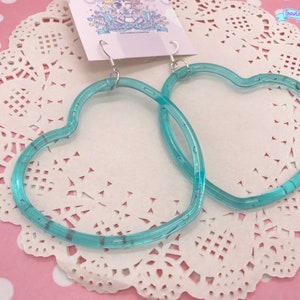 May include: A pair of turquoise heart-shaped hoop earrings. The earrings are made of clear plastic with a subtle shimmer.
