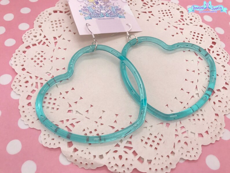 May include: A pair of turquoise heart-shaped hoop earrings. The earrings are made of clear plastic with a subtle shimmer.