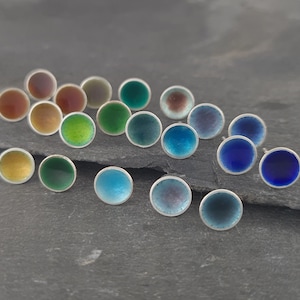 May include: Assortment of colourful enamel earrings in various shades of blue, green, brown, and yellow. The earrings are round and have a silver backing.