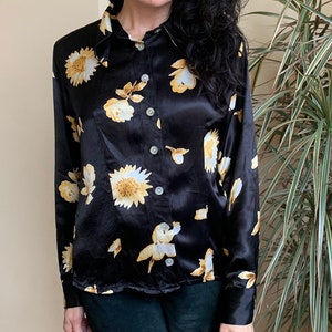 May include: A black satin blouse with a floral print featuring yellow and white sunflowers. The blouse has a collared neckline and long sleeves.