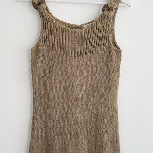 May include: A sleeveless, knitted tank top in a light brown color. The top has a scoop neck and features two brown, knotted straps with decorative rings.