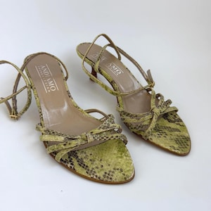 May include: A pair of lime green and brown snakeskin print sandals with a pointed toe, thin straps, and a low kitten heel. The insole features the text ANDIAMO printed in white. The shoes include an adjustable ankle strap with a gold buckle.