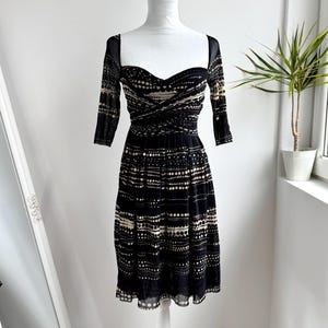 May include: Black and beige patterned dress with a sweetheart neckline and three-quarter sleeves. The dress features a fitted bodice and a flared skirt, displayed on a white dress form. The dress has a delicate, semi-sheer overlay.
