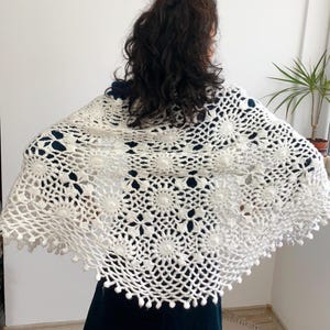 May include: White crocheted shawl with a delicate floral pattern and a scalloped edge. The shawl is made with a fine yarn and has a soft, airy feel.