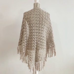 Könnte beinhalten: Ein beigefarbener Häkel-Schal mit Fransen an den Rändern. Der Schal wird auf einer weißen Schaufensterpuppe präsentiert.