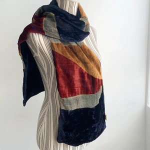 Può includere: Una sciarpa di velluto blu, rosso, marrone e verde con un motivo geometrico.