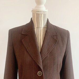 May include: A brown blazer with thin vertical stripes. The blazer has a single button closure and a notched lapel.