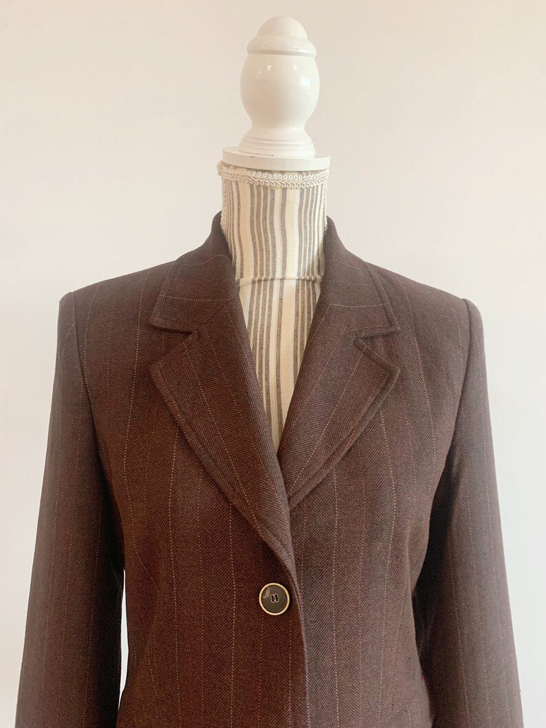 May include: A brown blazer with thin vertical stripes. The blazer has a single button closure and a notched lapel.