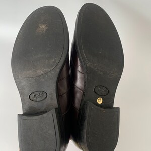 K&ouml;nnte beinhalten: Ein Paar braune Lederschuhe mit schwarzer Gummisohle. Die Schuhe haben eine spitze Zehenpartie und einen niedrigen Absatz. Die Sohlen sind mit "Made in Italy" und "39" gekennzeichnet.