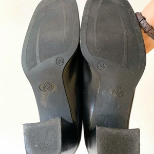 May include: A pair of black leather shoes with square toes and block heels. The soles are visible, showing size 38 and a textured pattern. The heels are approximately 2 inches high.