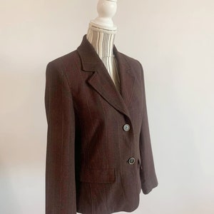 May include: A brown blazer with thin vertical stripes. The blazer has a notched collar, two button closure, and two front pockets.
