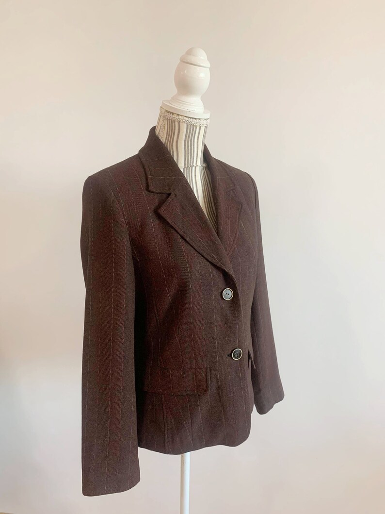 May include: A brown blazer with thin vertical stripes. The blazer has a notched collar, two button closure, and two front pockets.