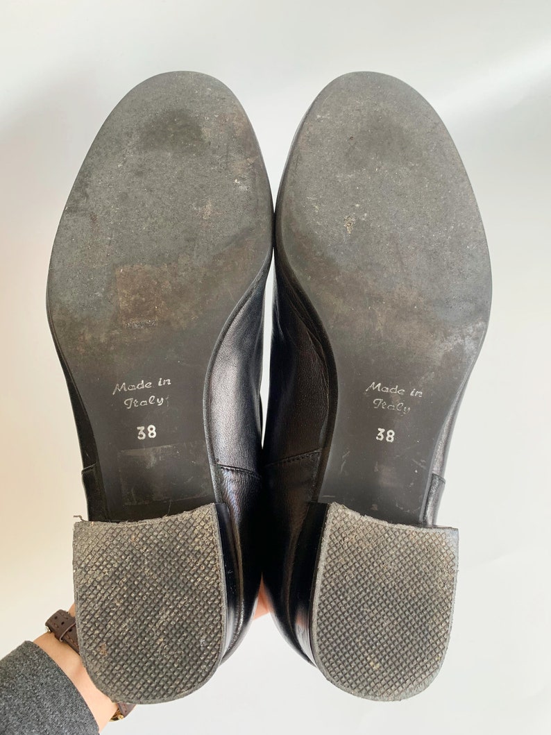 Pu&ograve; includere: Primo piano delle suole di un paio di stivaletti in pelle nera. Gli stivaletti hanno un tacco a blocco e sono etichettati "Made in Italy" e "38".
