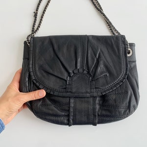 May include: Black leather shoulder bag with a chain strap and a decorative ruffle detail.