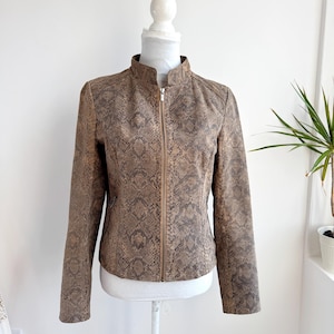 Op de afbeelding: Een bruine imitatie leren jas met een slangenprint. De jas heeft een opstaande kraag, een ritssluiting aan de voorkant en lange mouwen. Het wordt getoond op een witte mannequin tegen een witte achtergrond.
