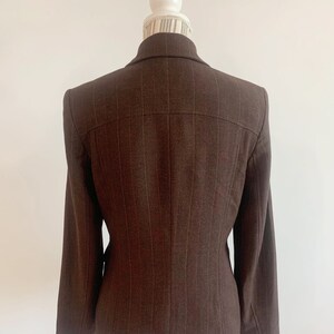 May include: A brown blazer with thin vertical stripes. The blazer has a single-breasted closure and long sleeves.