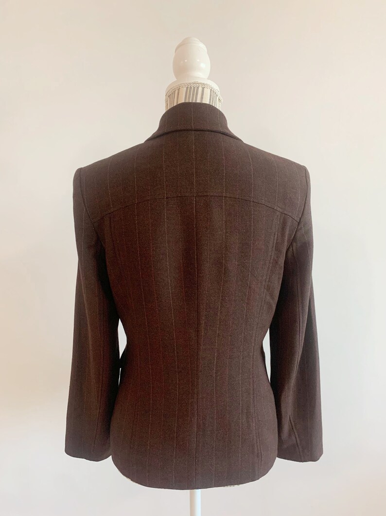 May include: A brown blazer with thin vertical stripes. The blazer has a single-breasted closure and long sleeves.