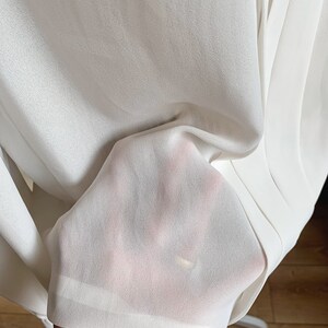 Puede incluir: Tela blanca transparente con una textura suave. La tela est&aacute; doblada y drapeada, mostrando su naturaleza delicada y fluida.