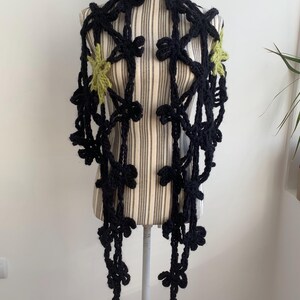 May include: A black crocheted scarf with green star accents. The scarf is displayed on a white mannequin.