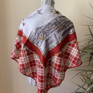 May include: A white and red silk scarf with a plaid pattern and a print of ducks flying over a landscape.
