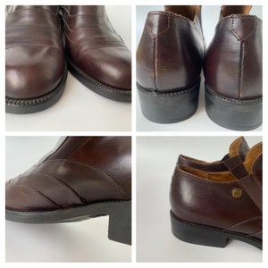 K&ouml;nnte beinhalten: Ein Paar braune Lederstiefeletten mit spitzer Zehenpartie und niedrigem Absatz. Die Stiefeletten haben einen Rei&szlig;verschluss an der Innenseite des Kn&ouml;chels und einen dekorativen Riemen &uuml;ber dem Fu&szlig;r&uuml;cken.