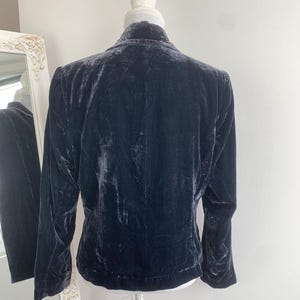 May include: A dark navy blue velvet blazer displayed on a mannequin. The blazer has long sleeves and a classic collar. The fabric has a soft, textured appearance. The blazer is a sophisticated piece of apparel.